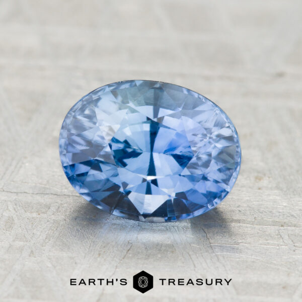 2.49-Carat Ceylon Sapphire (Heated) 2.49-carat Ceylon Sapphire (heated), oval-cut and blue, showcased on a textured gray surface with "Earth's Treasury" displayed at the bottom.