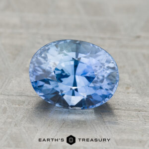 2.49-carat Ceylon Sapphire (heated), oval-cut and blue, showcased on a textured gray surface with "Earth's Treasury" displayed at the bottom.