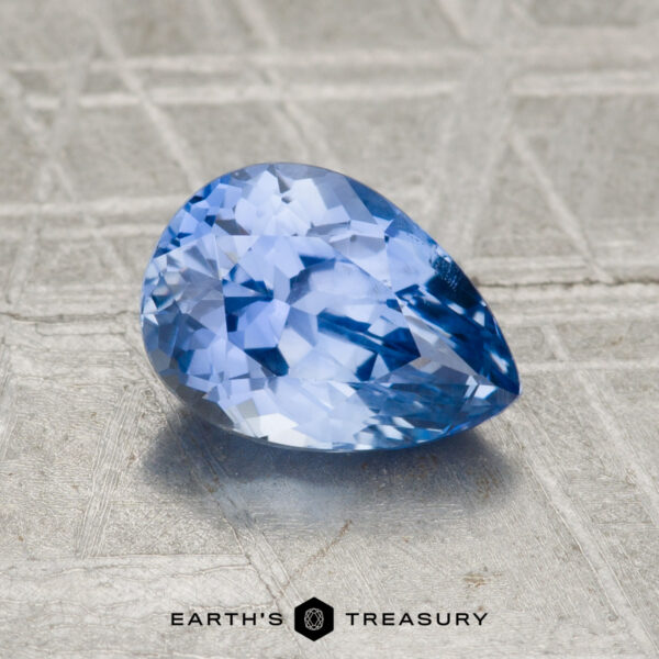 1.55-Carat Ceylon Sapphire A 1.55-carat Ceylon sapphire, cut in a pear shape with facets, is displayed on a textured surface with "EARTH'S TREASURY" written below.