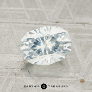 A 1.80-carat Montana Sapphire with an oval brilliant cut is showcased on a textured gray surface, featuring the text "Earth's Treasury" at the bottom.