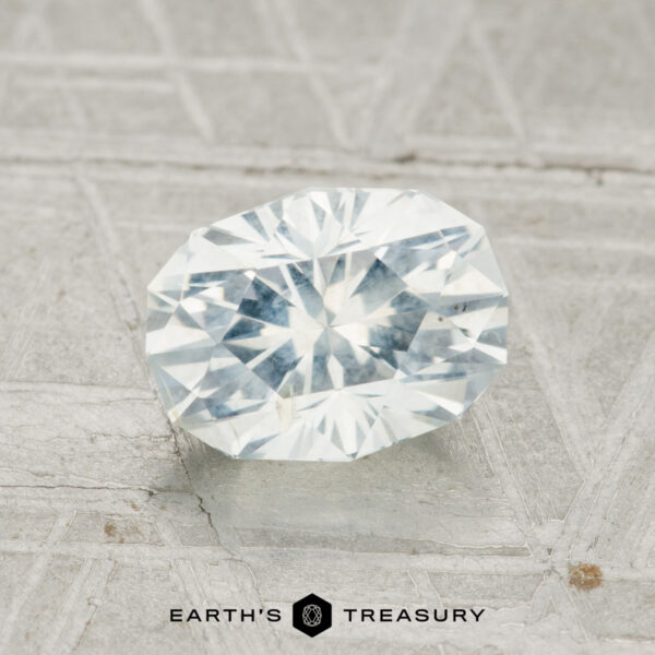 1.80-Carat Montana Sapphire A 1.80-carat Montana Sapphire with an oval brilliant cut is showcased on a textured gray surface, featuring the text "Earth's Treasury" at the bottom.