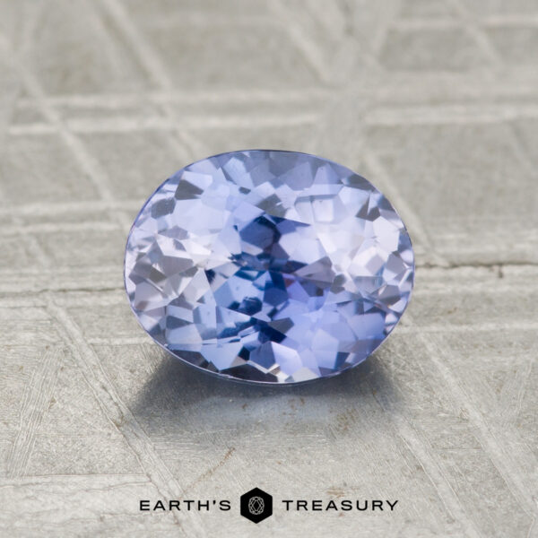 1.41-Carat Ceylon Sapphire A 1.41-carat Ceylon sapphire, oval-cut and light blue, rests on a textured metallic surface with "EARTH'S TREASURY" displayed below.