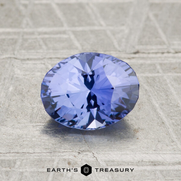 1.48-Carat Ceylon Sapphire A 1.48-carat Ceylon Sapphire in a faceted oval cut rests on a textured gray surface, with "Earth's Treasury" displayed at the bottom.
