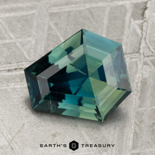 2.44-Carat Ceylon Sapphire (Heated) A 2.44-carat heated Ceylon sapphire with deep blue-green geometric facets rests on a textured gray surface; the Earth's Treasury logo is displayed below.