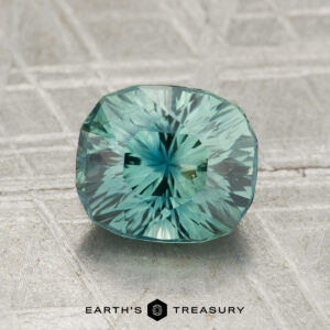 A 2.16-carat sapphire is displayed on a textured, pale surface with the text "EARTH'S TREASURY" at the bottom.