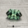 A 1.26-carat faceted hexagonal green sapphire rests on a textured gray surface with the "EARTH'S TREASURY" text and logo at the bottom of the image.