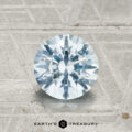 A 1.40-carat Montana sapphire in a round brilliant cut is displayed on a textured metallic surface with "EARTH'S TREASURY" at the bottom.