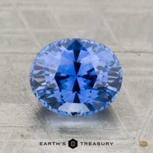 A 2.29-carat heated Ceylon sapphire with an oval cut is displayed on a textured surface, with "EARTH'S TREASURY" featured below.