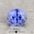 A faceted, oval-cut lavender-blue 2.29-carat heated Ceylon sapphire is displayed on a light textured surface with the text “EARTH’S TREASURY” beneath.