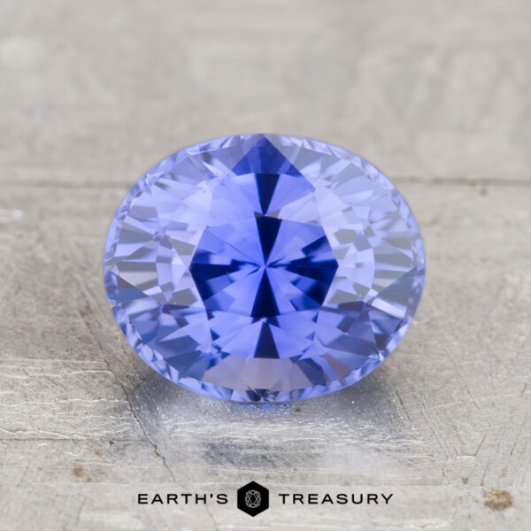 2.29-Carat Ceylon Sapphire (Heated) A faceted, oval-cut lavender-blue 2.29-carat heated Ceylon sapphire is displayed on a light textured surface with the text “EARTH’S TREASURY” beneath.