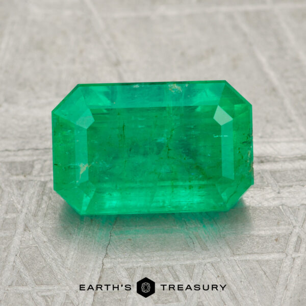 2.25-Carat Emerald A 2.25-carat rectangular-cut green emerald gemstone rests on a textured gray surface with "EARTH'S TREASURY" displayed at the bottom.