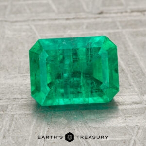 A 2.13-carat emerald-cut green gemstone is displayed on a light textured surface with the "Earth's Treasury" logo and text below.