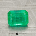 A 1.94-carat emerald-cut green gemstone is showcased on a textured gray surface with "EARTH'S TREASURY" text beneath it.