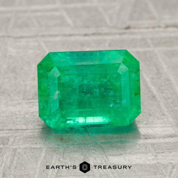 1.94-Carat Emerald A 1.94-carat emerald-cut green gemstone is showcased on a textured gray surface with "EARTH'S TREASURY" text beneath it.