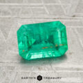 A 1.52-carat emerald-cut green gemstone is displayed on a textured gray surface, with the logo and text "EARTH'S TREASURY" below it.