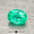 A 1.51-carat oval-cut green emerald gemstone rests on a textured gray surface, with the Earth's Treasury logo displayed at the bottom.