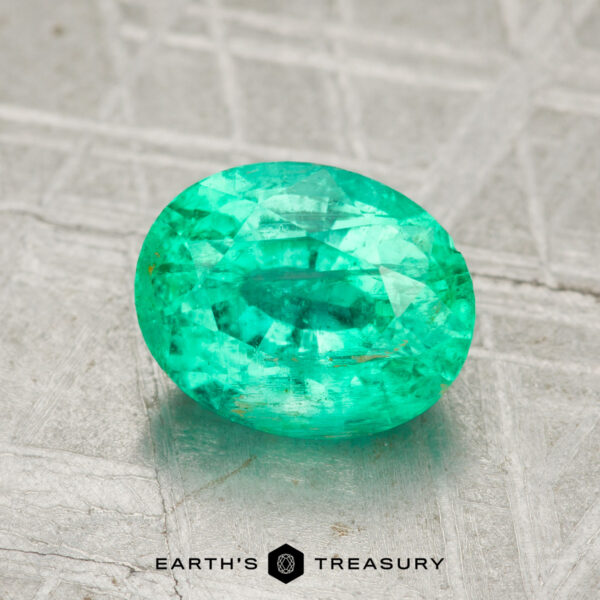 1.51-Carat Emerald A 1.51-carat oval-cut green emerald gemstone rests on a textured gray surface, with the Earth's Treasury logo displayed at the bottom.