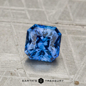 A 1.19-carat heated Ceylon sapphire with square cut and intricate faceting rests on a textured metallic surface, with the "Earth's Treasury" logo displayed below.