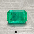 A 1.40-carat rectangular, faceted green emerald rests on a textured gray surface. "EARTH'S TREASURY" appears at the bottom of the image.