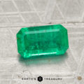 A 1.39-carat emerald-cut green gemstone rests on a textured metallic surface, with the logo and text "EARTH'S TREASURY" below.