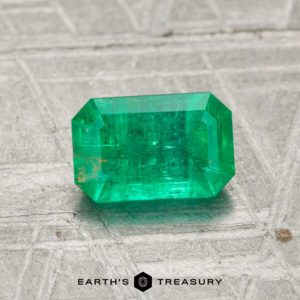 1.00-Carat Emerald A 1.00-carat emerald with a rectangular cut is placed on a textured gray surface, featuring the text "EARTH'S TREASURY" at the bottom.