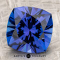 A faceted, vivid blue 40.58-carat Tanzanite gemstone with geometric cuts rests on a textured surface, labeled "EARTH'S TREASURY" at the bottom.