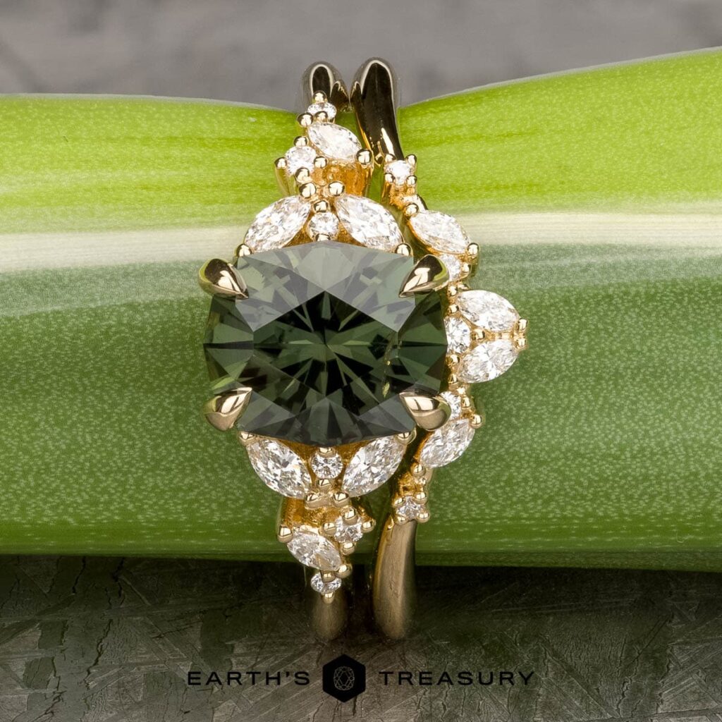 The holly ring features a vivid green gemstone set in a gold band with sparkling white diamond accents, displayed on a green plant stem—a distinctive and elegant wedding band choice.