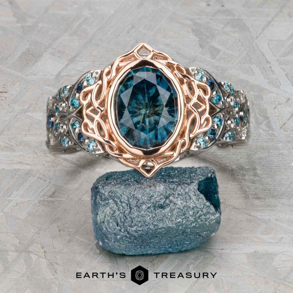 The Haupt, Jess and Limoncelli, Mary Anne 1 ring—a platinum and rose gold piece with a large blue gemstone and detailed design—is shown above a raw blue gemstone, with the Earth’s Treasury logo beneath.