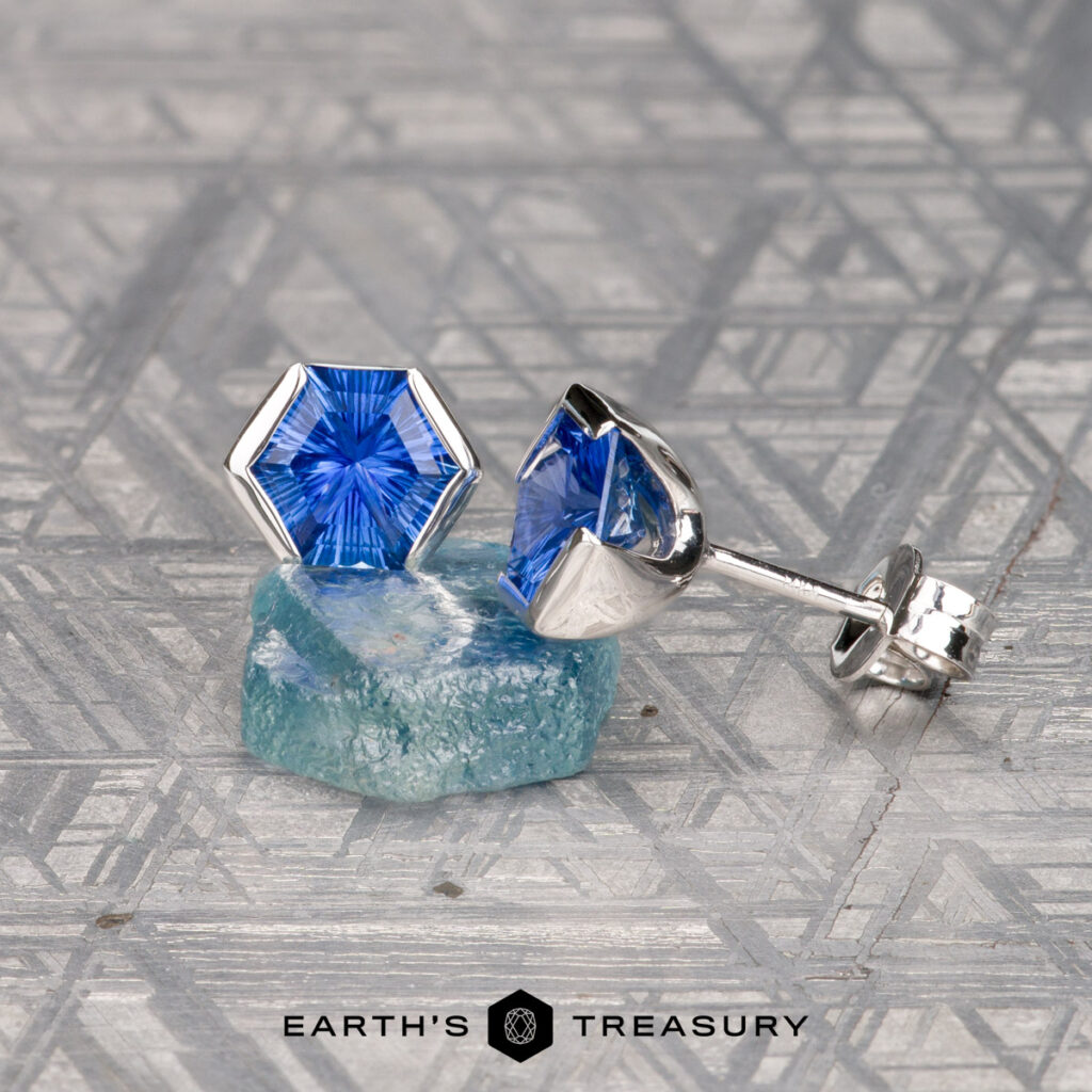 The Crookham, Ryan [custom gallery] features hexagonal blue gemstone stud earrings set in silver, paired with a rough blue stone on a geometric patterned surface.