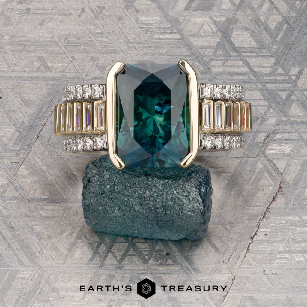 The Gaylord, Allison and Hermes, Robert 1 ring—a gold band featuring a large blue-green gemstone and diamonds—is displayed on a rough blue-green mineral, set against geometric-patterned backgrounds.