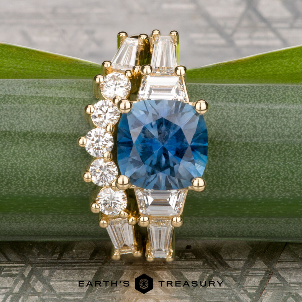 The Clifford, Barrie 1 & 2 wedding band set features a gold band with a central blue round gemstone, elegantly accented by baguette and round diamonds—an ideal choice for timeless elegance.