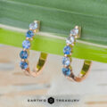 A pair of "Eclipse" Earrings in 14K rose gold rests on a green leaf, with the Earth's Treasury logo at the bottom.