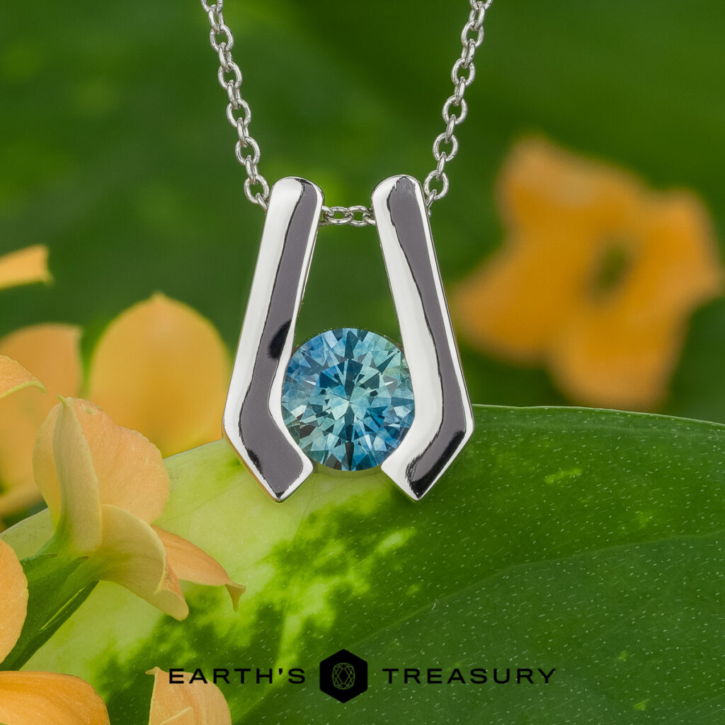 A silver pendant necklace with a round blue gemstone, "Stacked from 16 images. Method=B (R=7,S=2)", is displayed against a green leaf and orange flower background. The text "EARTH'S TREASURY" appears at the bottom.