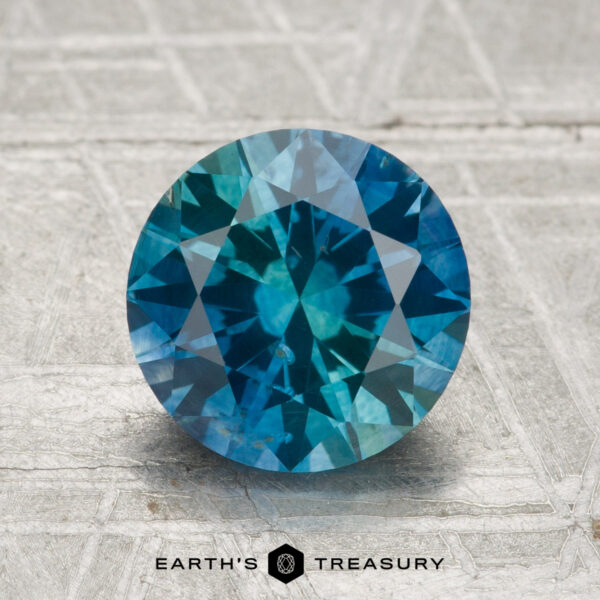 2.29-Carat Montana Sapphire (Heated) A round, faceted 2.29-carat Montana Sapphire (Heated) is displayed on a textured, light-colored surface with the text "EARTH'S TREASURY" at the bottom.