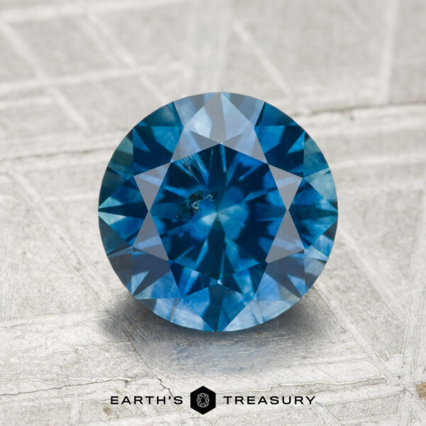2.18-Carat Montana Sapphire (Heated) A 2.18-carat heated Montana sapphire with a round brilliant cut rests on a textured metallic surface, with "Earth's Treasury" displayed below.