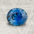 A 2.08-carat round, faceted blue sapphire is displayed on a textured gray surface with the "Earth's Treasury" logo at the bottom.
