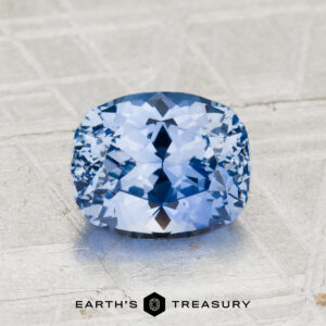 A faceted, cushion-cut 2.20-Carat Ceylon Sapphire rests on a textured gray surface with the text "EARTH'S TREASURY" below. This dazzling gemstone captivates with its vivid hue and exceptional clarity.