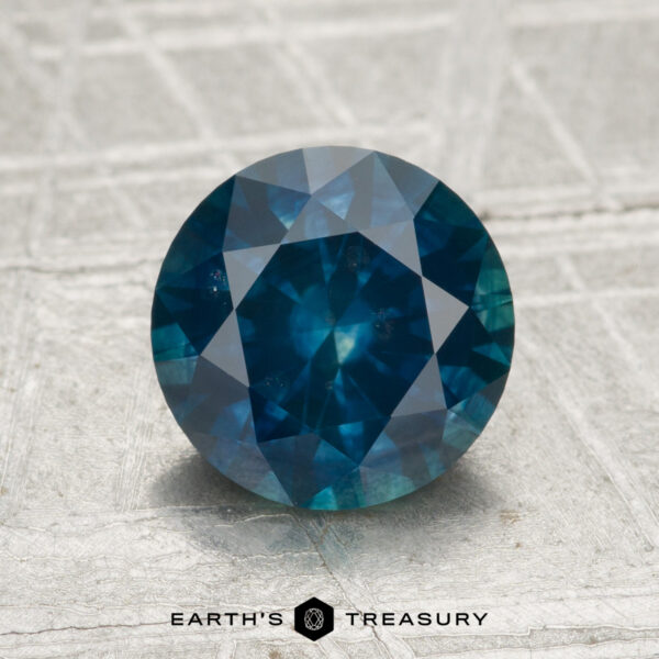 2.06-Carat Montana Sapphire (Heated) A 2.06-carat heated Montana sapphire, round-cut and blue, is shown on a light textured surface with "EARTH'S TREASURY" displayed at the bottom.