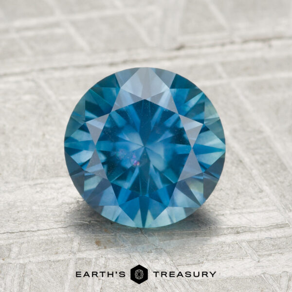 2.04-Carat Montana Sapphire (Heated) A 2.04-carat heated Montana sapphire, round brilliant-cut, is displayed on a textured surface with "EARTH'S TREASURY" at the bottom.