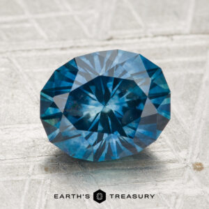 2.89-carat heated Montana sapphire, faceted oval blue gemstone shown on a textured surface with "Earth’s Treasury" at the bottom.