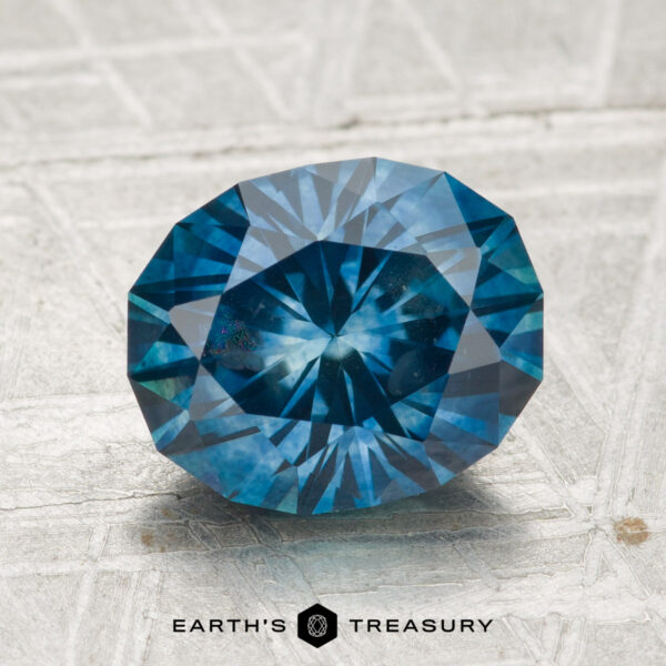 2.89-Carat Montana Sapphire (Heated) 2.89-carat heated Montana sapphire, faceted oval blue gemstone shown on a textured surface with "Earth’s Treasury" at the bottom.