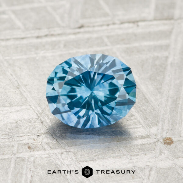 1.25-Carat Montana Sapphire (Heated) A 1.25-carat heated Montana sapphire is displayed on a light textured surface with the text "EARTH'S TREASURY" and a logo at the bottom.