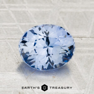 A 2.24-carat Ceylon Sapphire, round brilliant-cut and blue, is displayed on a textured metallic surface with the "EARTH'S TREASURY" logo and text at the bottom.