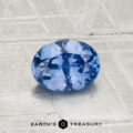 A 1.04-carat Ceylon Sapphire, faceted and oval-shaped, is displayed on a textured light gray surface with the "EARTH'S TREASURY" logo at the bottom.