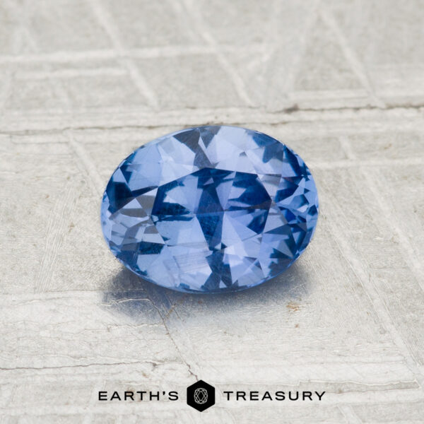 1.04-Carat Ceylon Sapphire A 1.04-carat Ceylon Sapphire, faceted and oval-shaped, is displayed on a textured light gray surface with the "EARTH'S TREASURY" logo at the bottom.