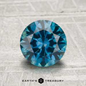 A 1.88-carat heated Montana sapphire, round brilliant-cut, is displayed on a textured surface with "Earth's Treasury" below it.