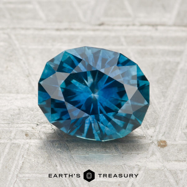 2.39-Carat Montana Sapphire (Heated) A 2.39-carat heated Montana sapphire, faceted in an oval shape, is displayed on a gray textured surface with the text "EARTH'S TREASURY" at the bottom.