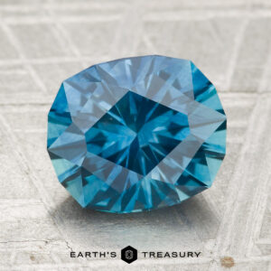 A 3.60-carat heated Montana sapphire is displayed on a textured surface with the "Earth's Treasury" logo and text at the bottom.