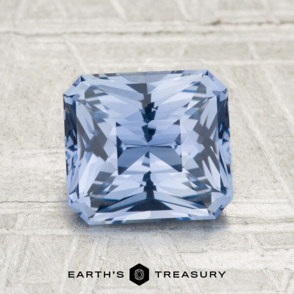 A 2.32-carat Ceylon sapphire, square-cut with intricate facets, rests on a textured gray surface. The "EARTH'S TREASURY" logo and text are featured at the bottom.
