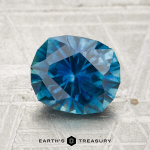 A 2.35-carat heated Montana sapphire is displayed on a textured surface with the Earth's Treasury logo and name at the bottom.